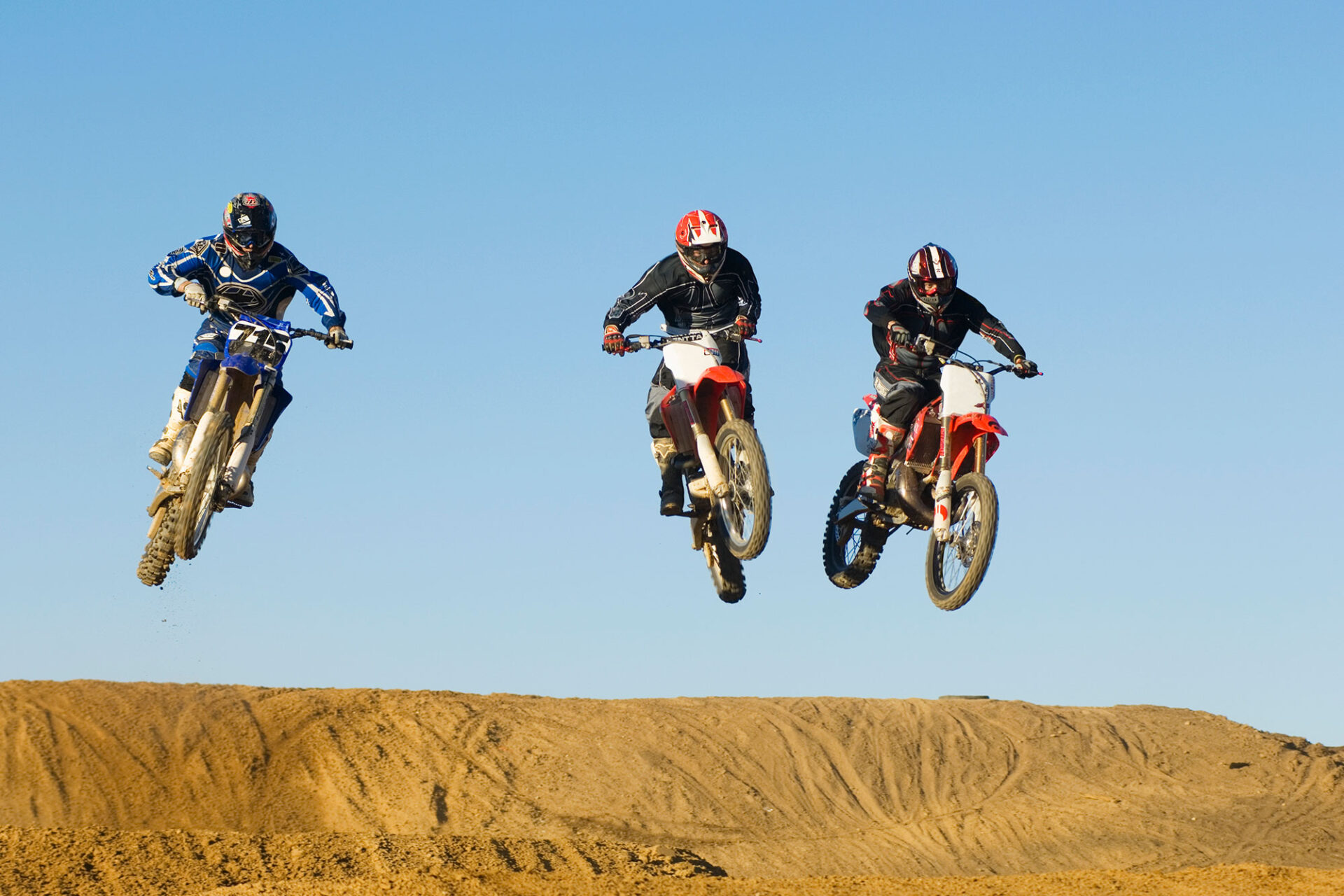 Three motocross male racers racing against clear blue sky